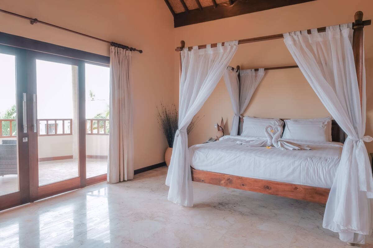 A bedroom with a wooden bed, white bedding, and sheer curtains.