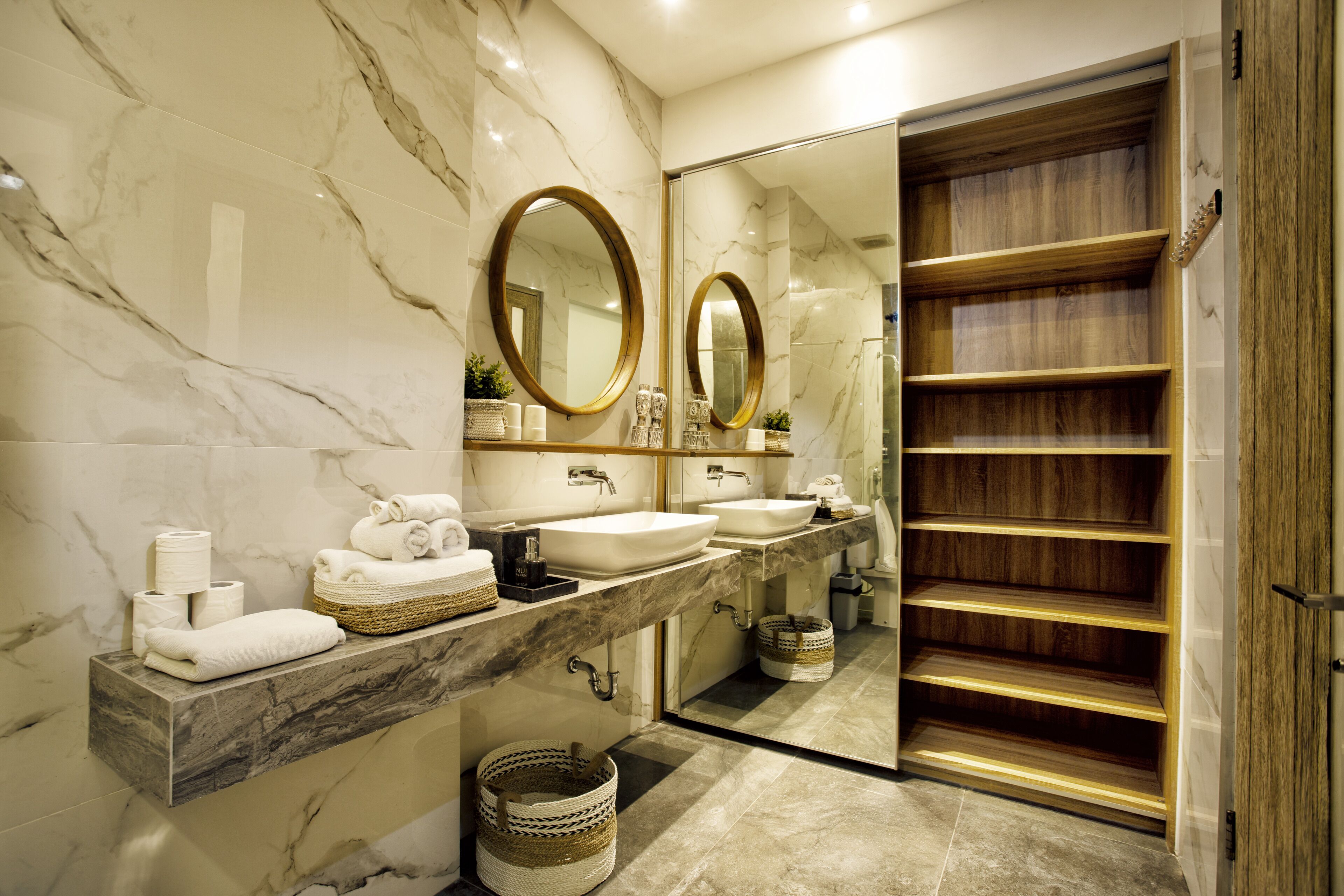 A modern bathroom with marble countertops, two sinks, a large mirror, and a wooden vanity with shelves.