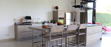 Una cocina moderna con una isla central, electrodomésticos de acero inoxidable y un comedor con sillas de metal.