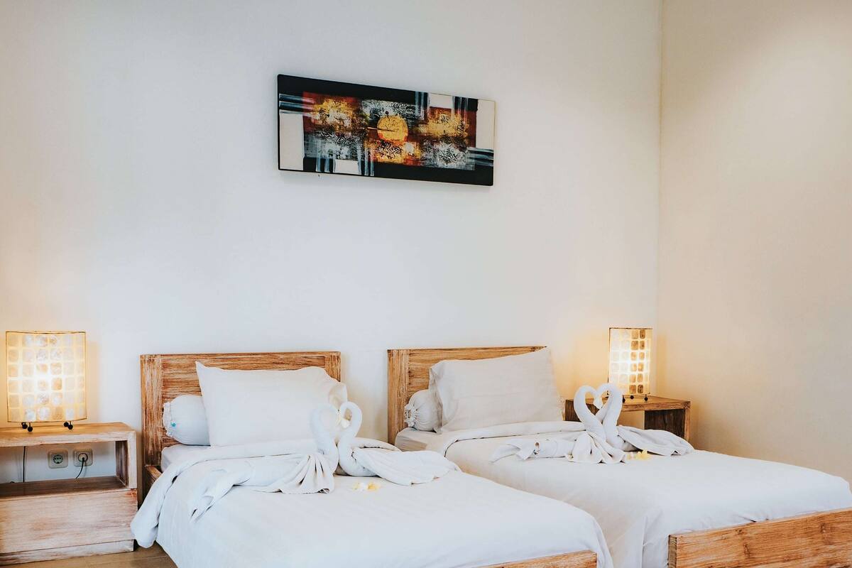 A hotel room with two wooden beds, white linens, and a painting on the wall.