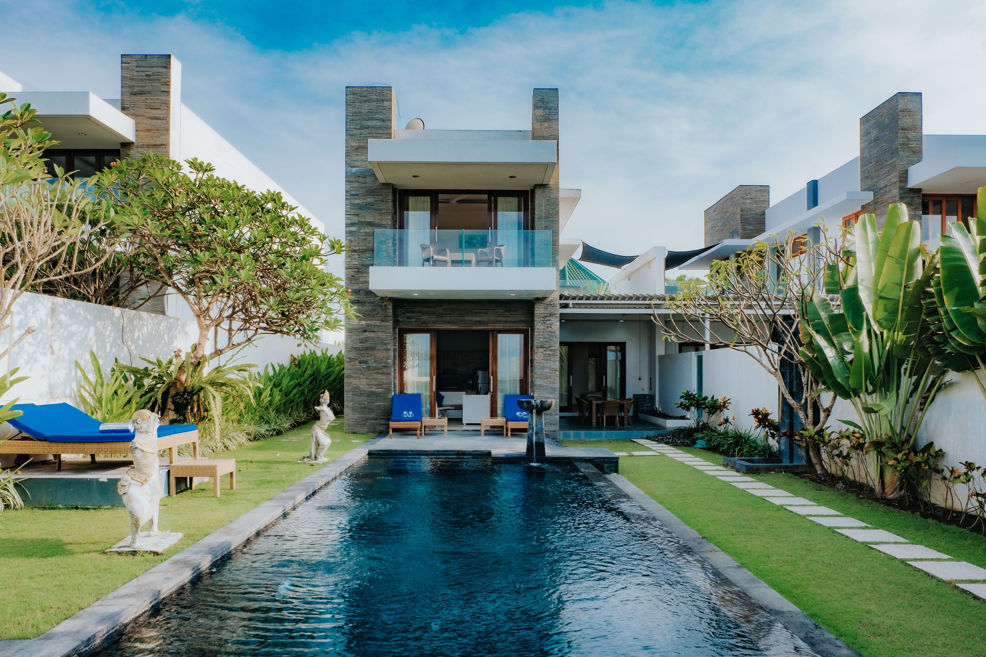 A modern two-story house with a swimming pool, outdoor seating, and lush landscaping.