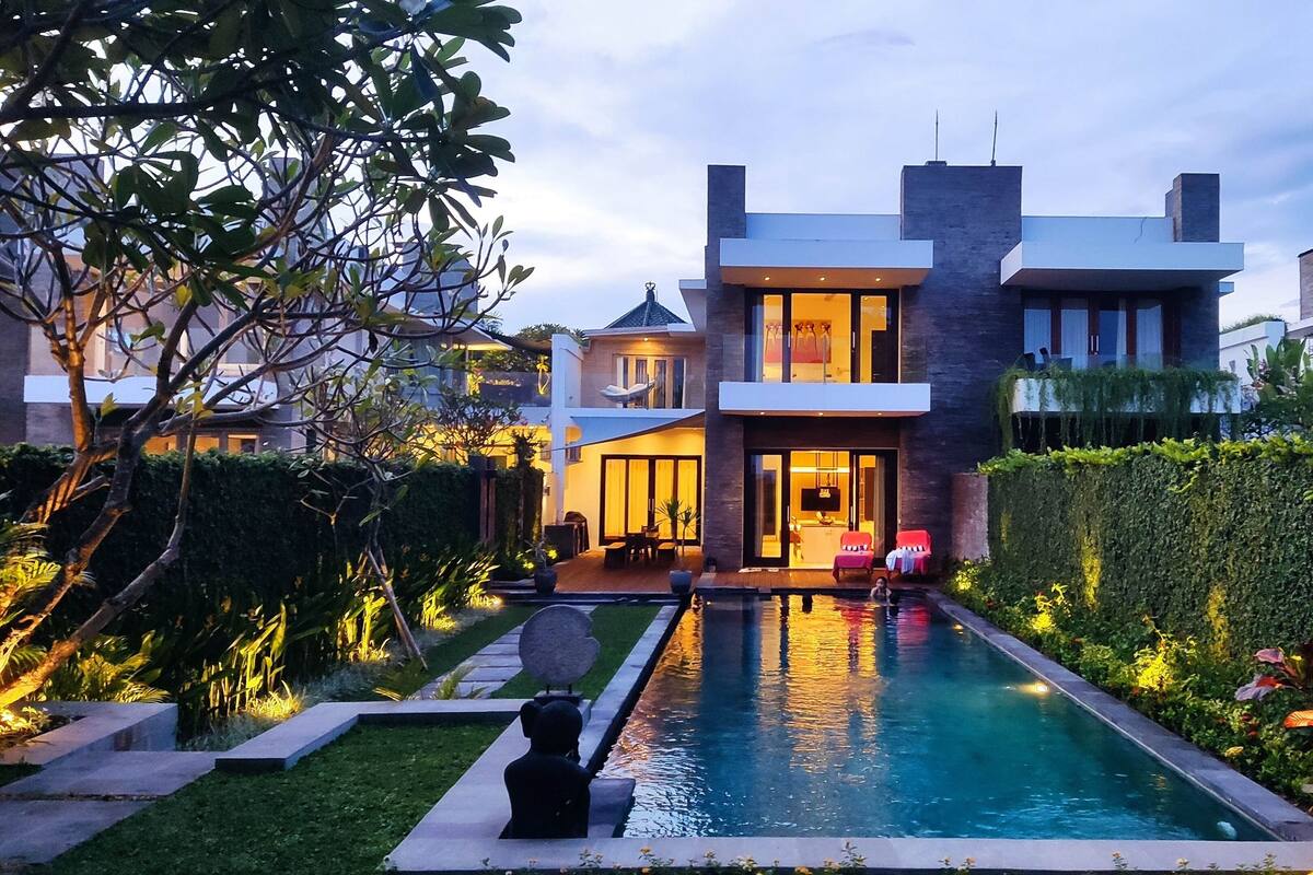 A modern two-story house with a swimming pool, surrounded by well-maintained gardens and a hedge.