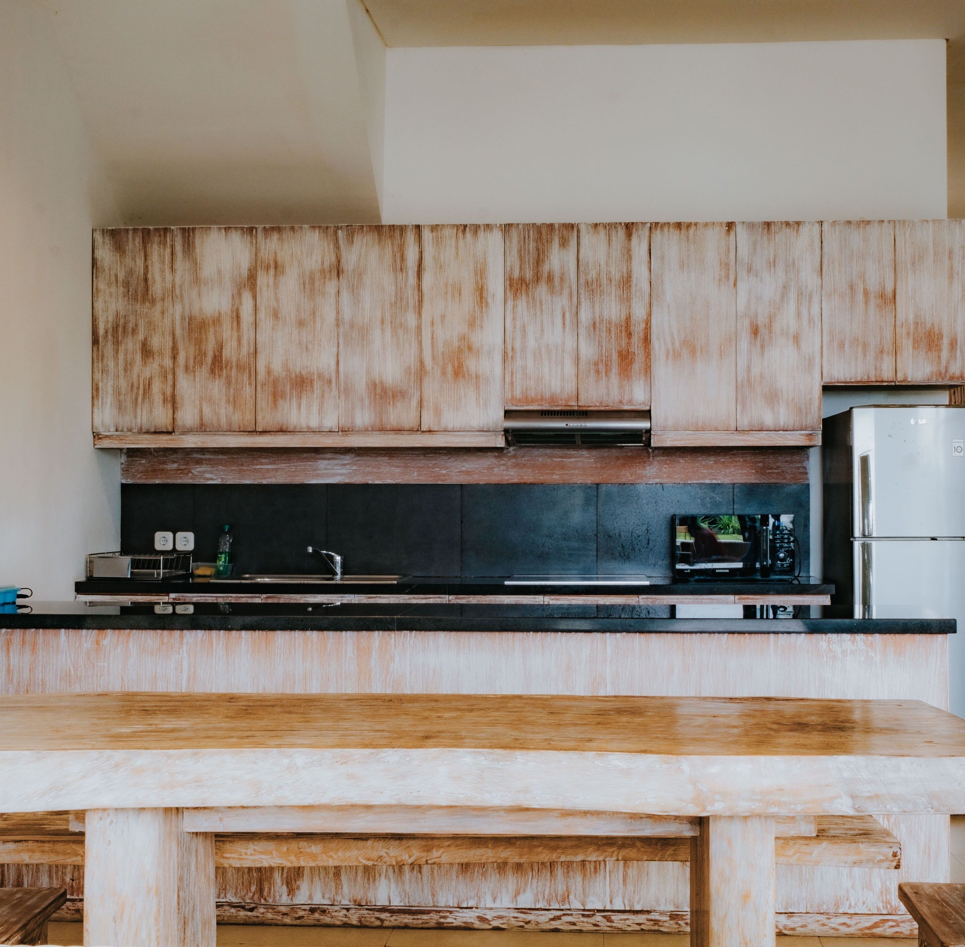 Una cocina con gabinetes de madera, encimera negra y refrigerador de acero inoxidable.