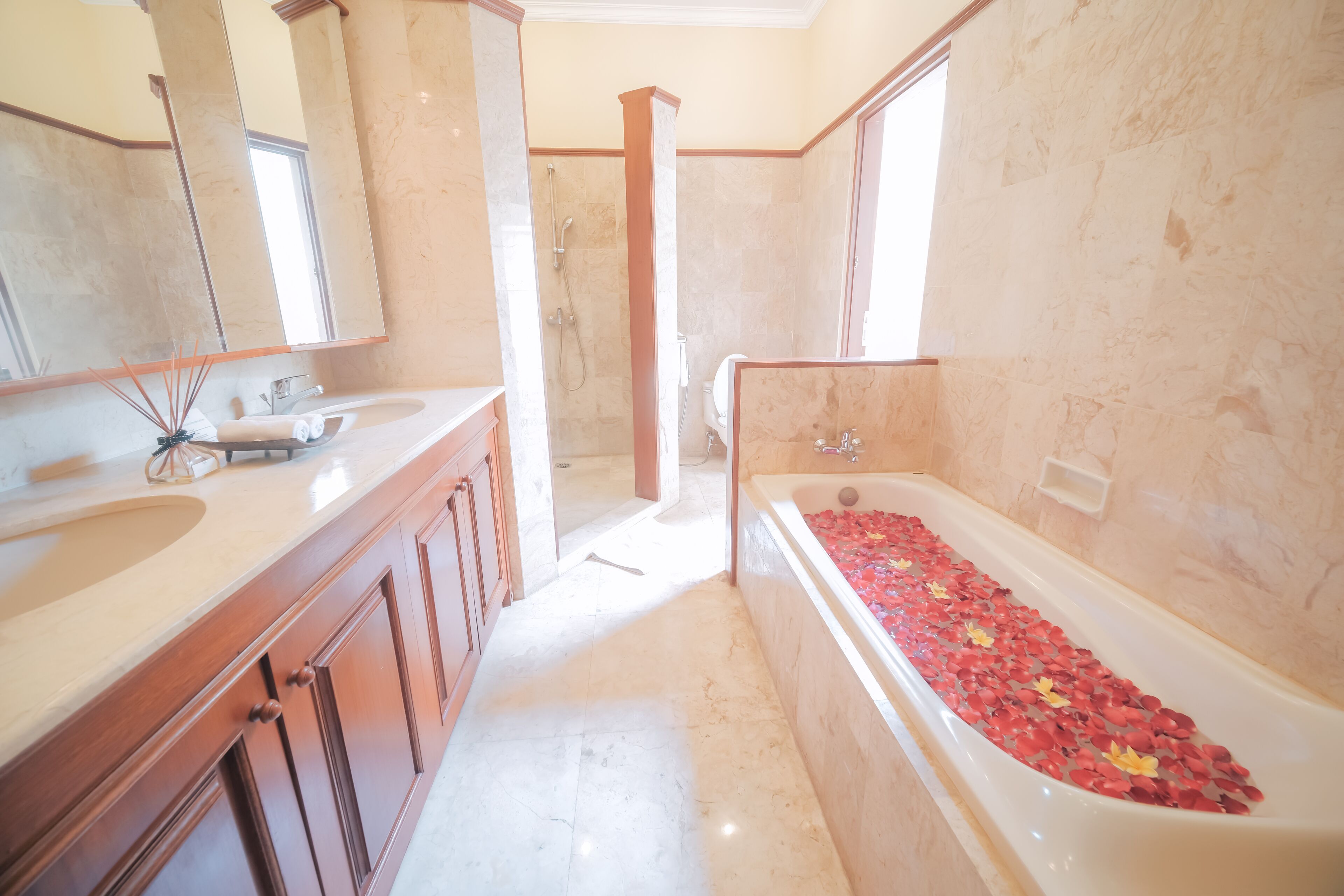 A bathroom with a bathtub filled with rose petals, a shower area, and a vanity with a mirror.