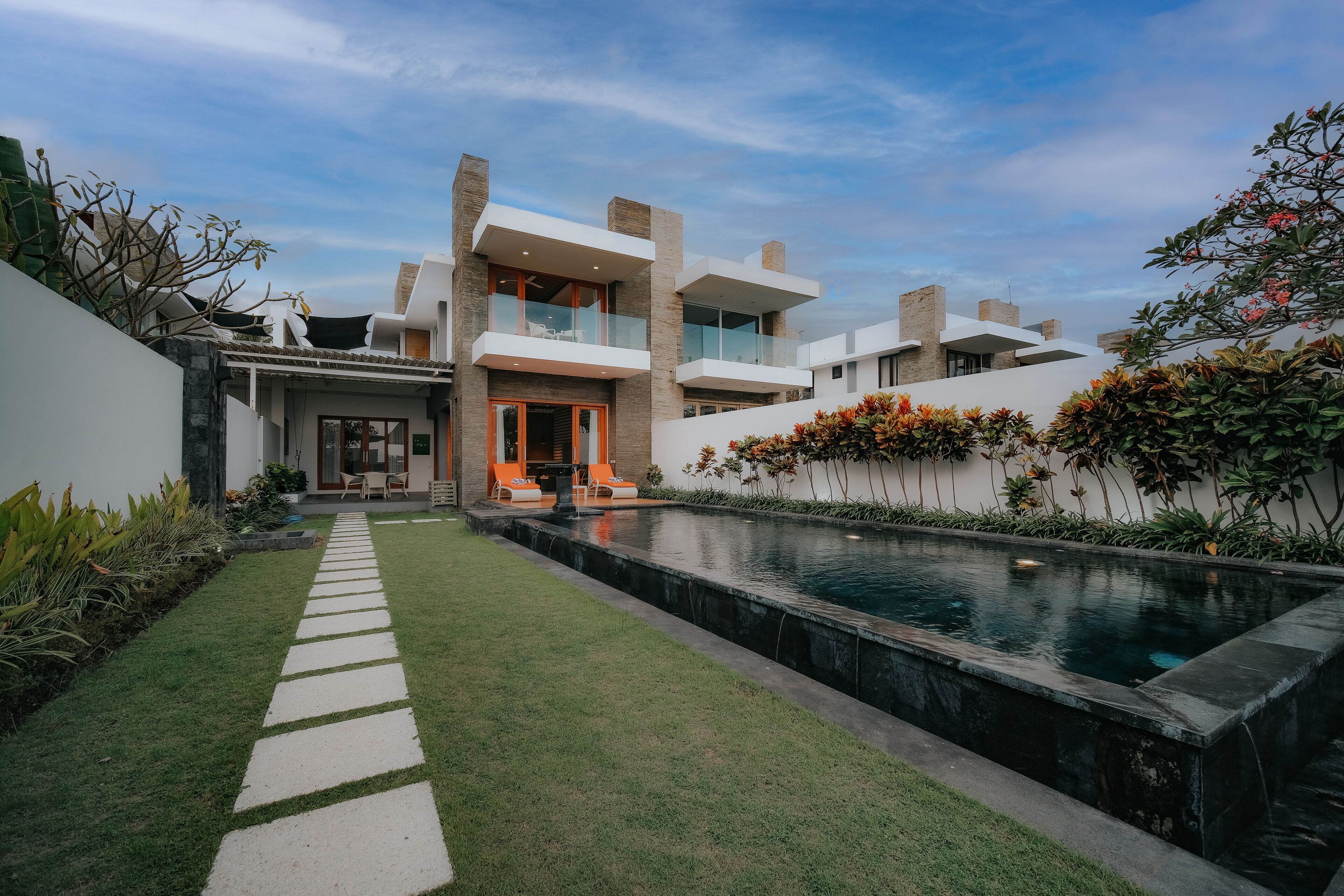 A modern house with a swimming pool, a paved pathway, and outdoor seating.