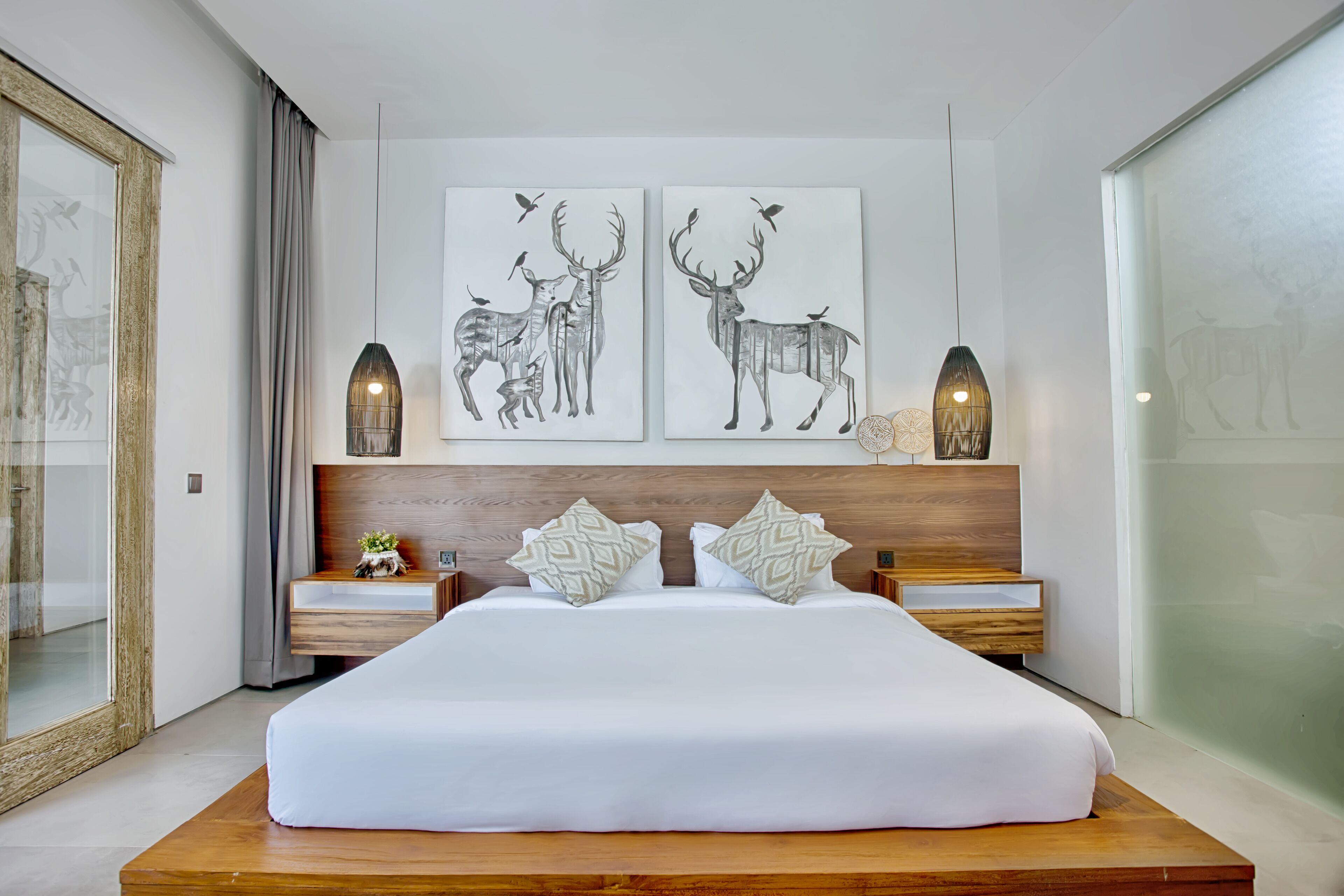 A modern hotel room with a large bed, two nightstands, and artwork depicting deer and birds.