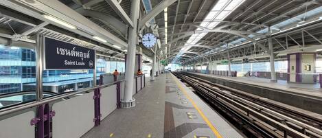 A train station platform with overhead tracks, a clock, and directional arrows on the floor.