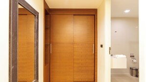 Une porte double en bois avec une poignée, un miroir sur le côté gauche, et une salle de bain blanche où l’on aperçoit des toilettes et une poubelle.