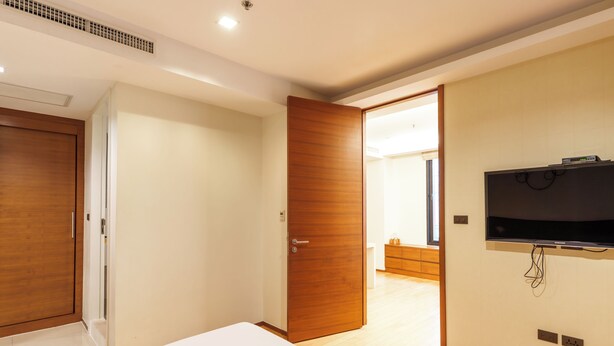 Une chambre d’hôtel moderne avec un grand lit, des portes en bois, un téléviseur fixé au mur et une vue sur la chambre adjacente.