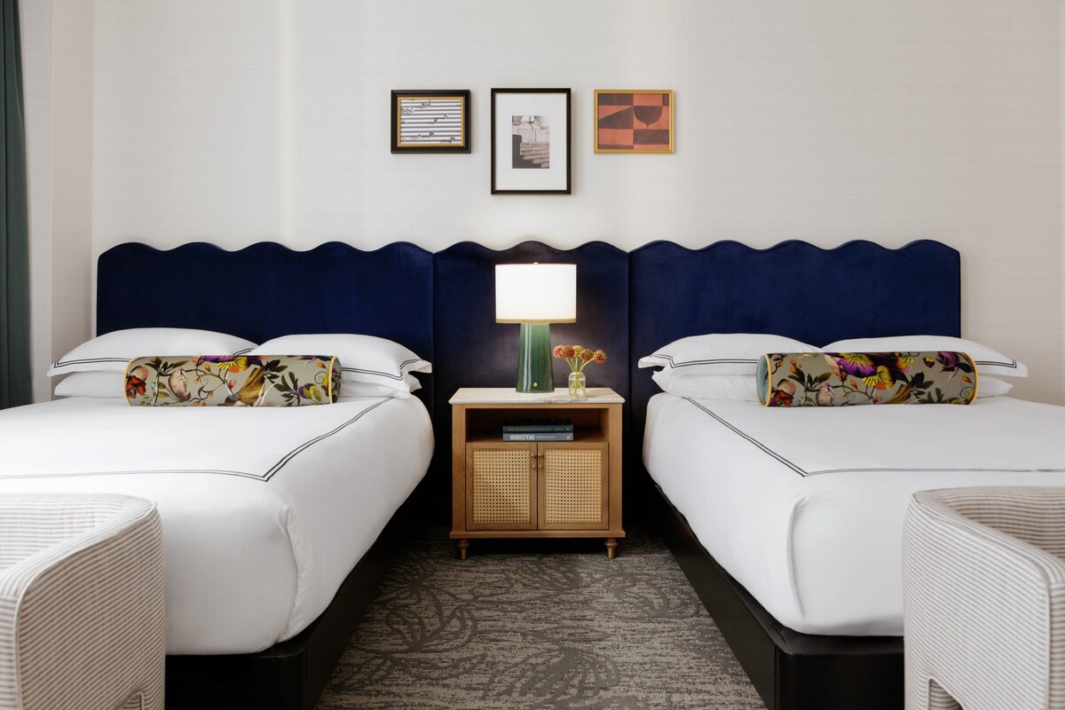 A hotel room with two beds, a nightstand with a lamp, and framed pictures on the wall.