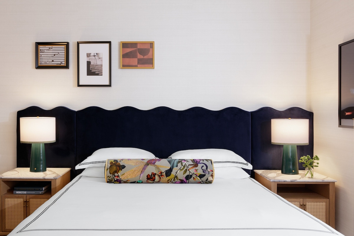 A hotel room with a large bed, two bedside tables with lamps, a headboard, and three framed pictures on the wall.
