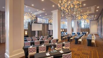 A conference room with tables and chairs, a large chandelier, and a screen.