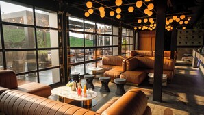 Un espace de détente moderne avec des canapés en cuir, une table basse et des luminaires suspendus. De grandes fenêtres offrent une vue sur l’extérieur.