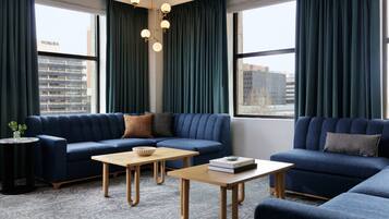 Una sala de estar moderna con un sofá azul, dos mesas de madera y vistas a un paisaje urbano a través de amplios ventanales.