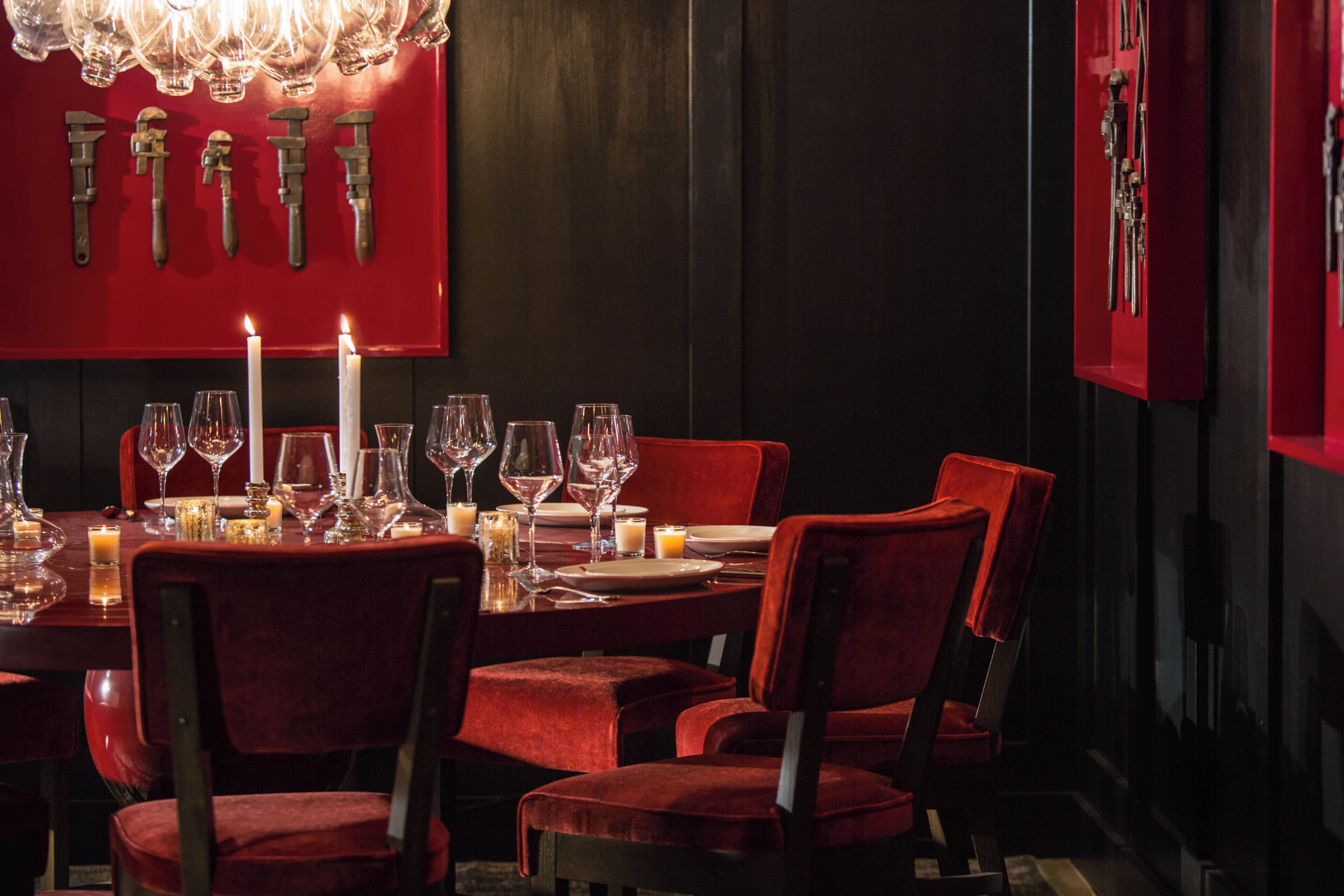 A dimly lit dining area with a red wall, a chandelier, and a table set for a meal.