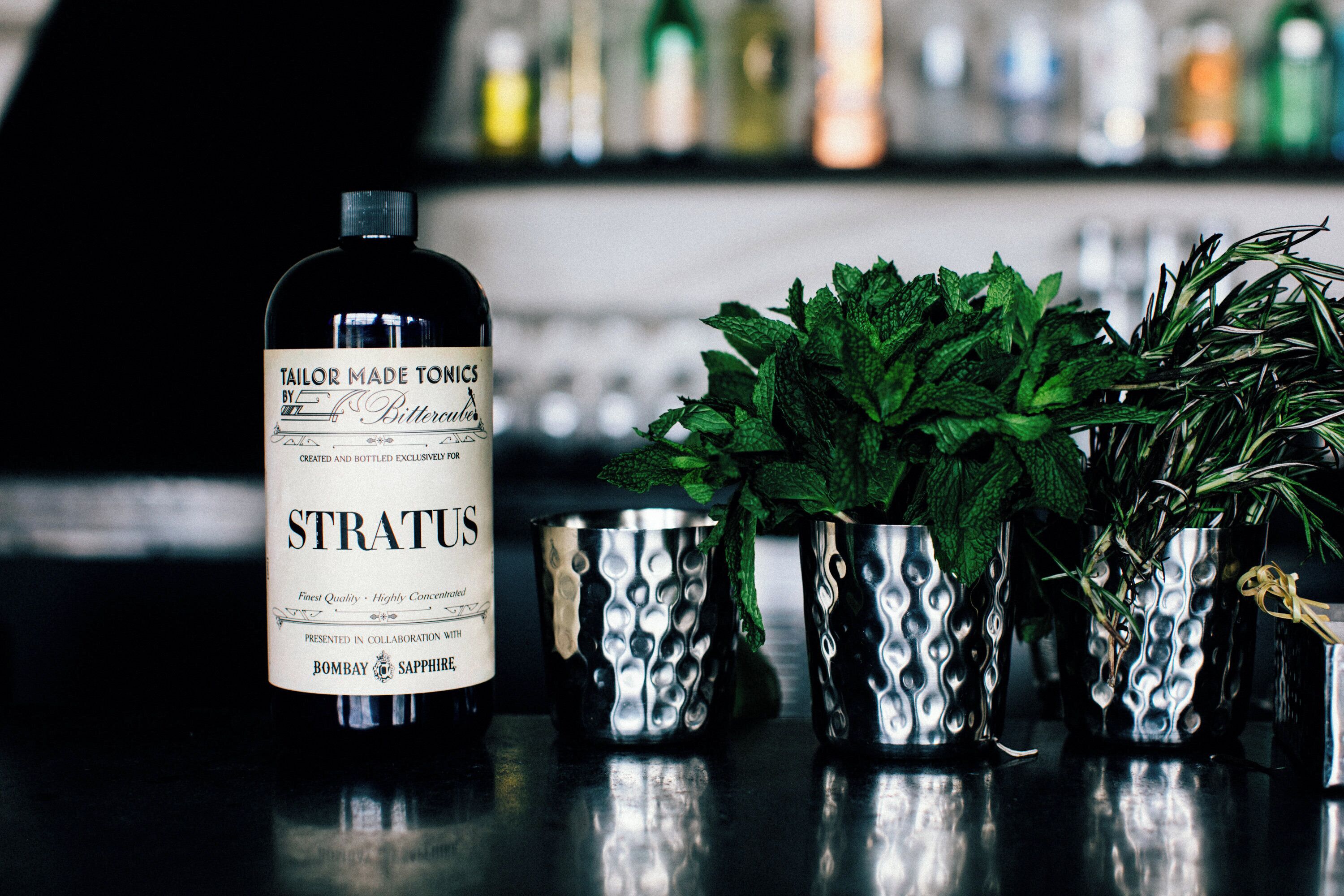 A bottle of STRATUS gin with a label, placed next to a metal cup with mint leaves.