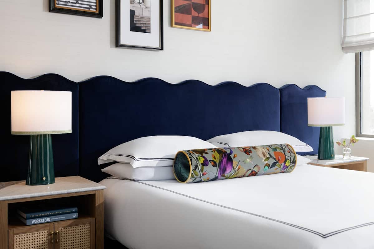 A neatly made bed with a decorative pillow, two bedside tables with lamps, a framed picture on the wall, and a small bookshelf.