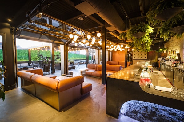 Un área de bar moderna con asientos de cuero, una barra y plantas colgantes.