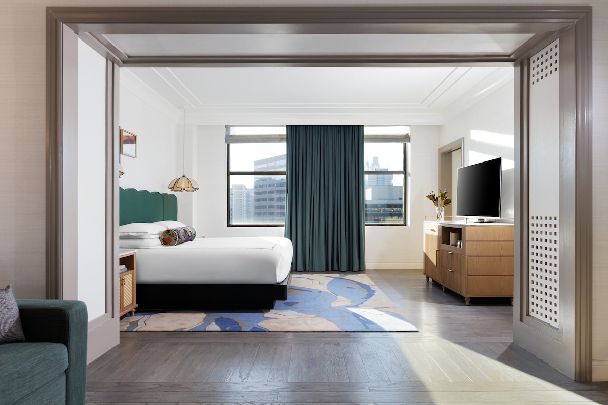 A hotel room with a bed, a television, a dresser, and a window with curtains.