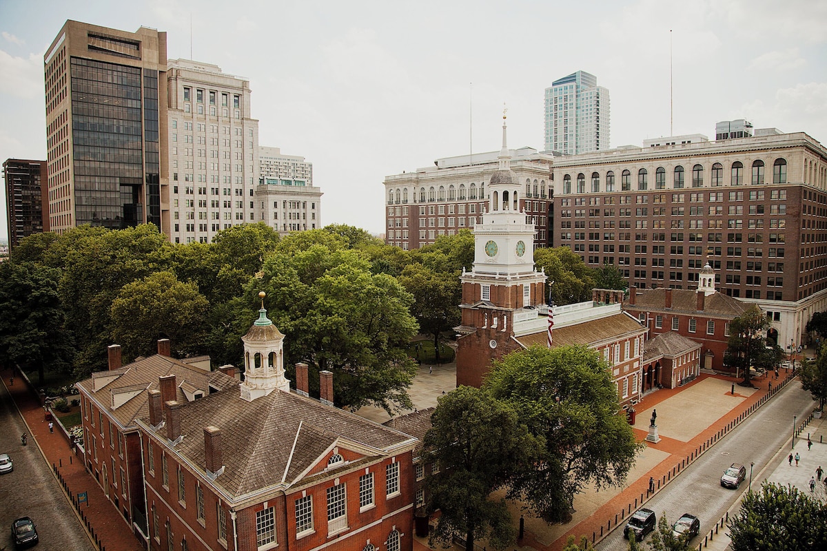 A historic building with a clock tower, surrounded by trees and modern high-rise buildings.