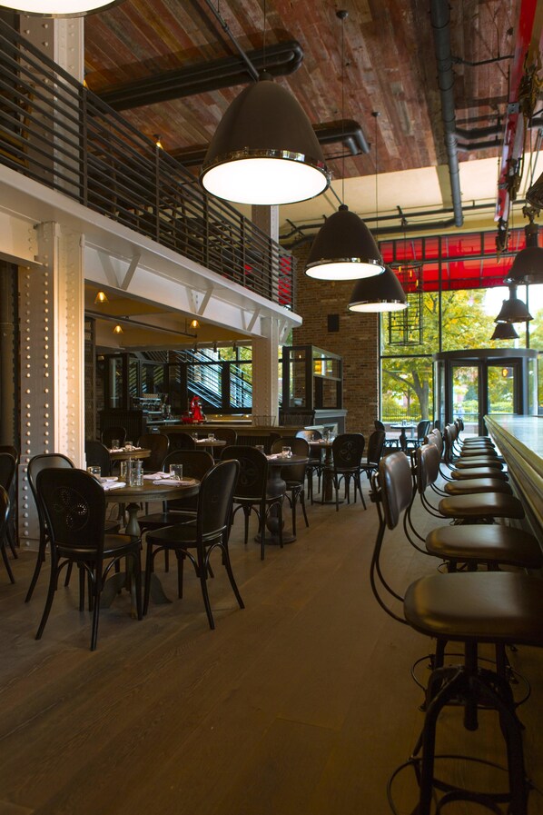 A restaurant with high ceilings, exposed beams, and a long counter with bar stools. Tables are arranged for dining, and there are hanging pendant lights. - Kimpton Hotel Monaco Philadelphia by IHG (Philadelphia)