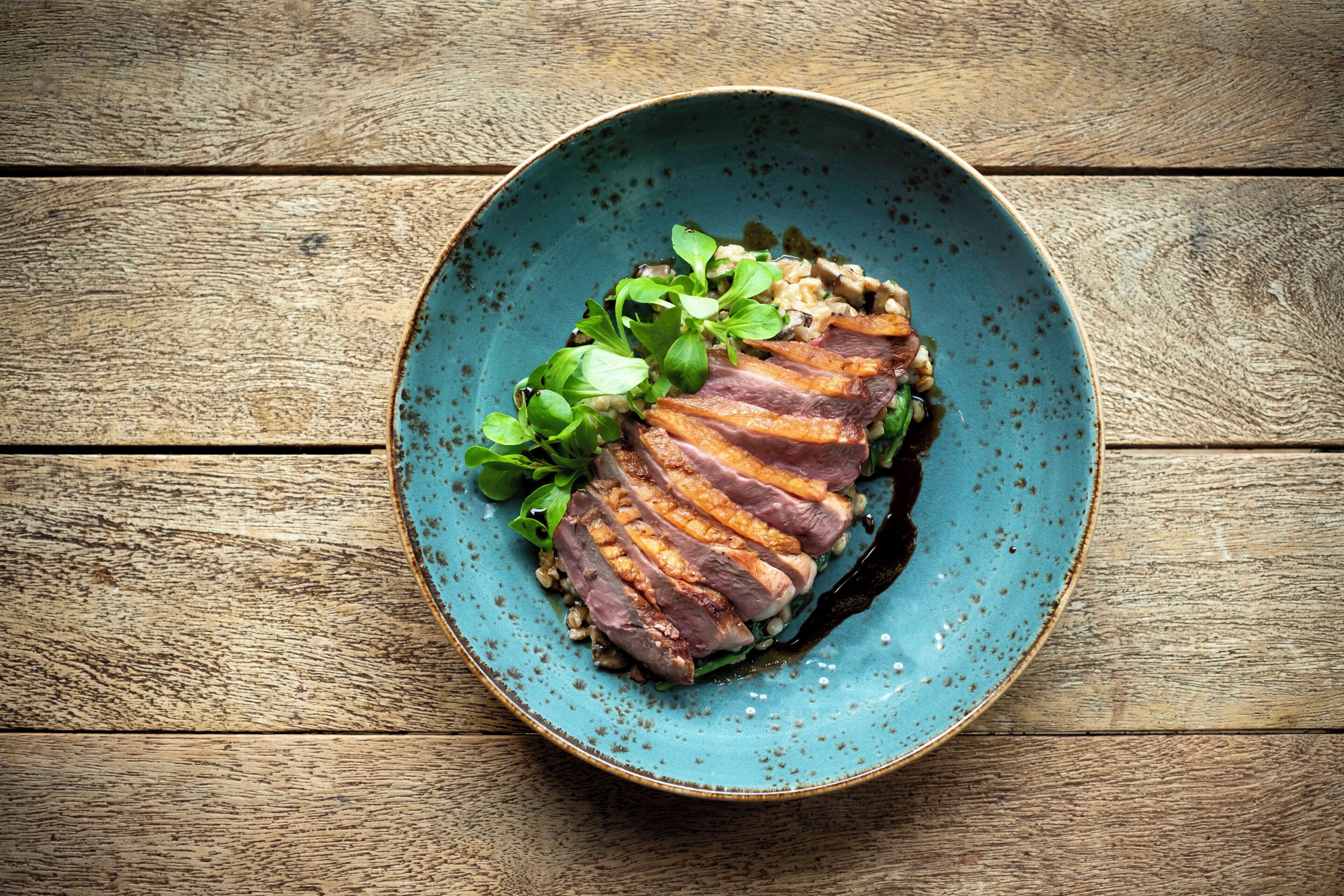 A plate of food with meat and greens on a wooden table.