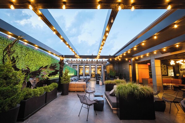 An outdoor patio with seating, a green wall, and string lights.