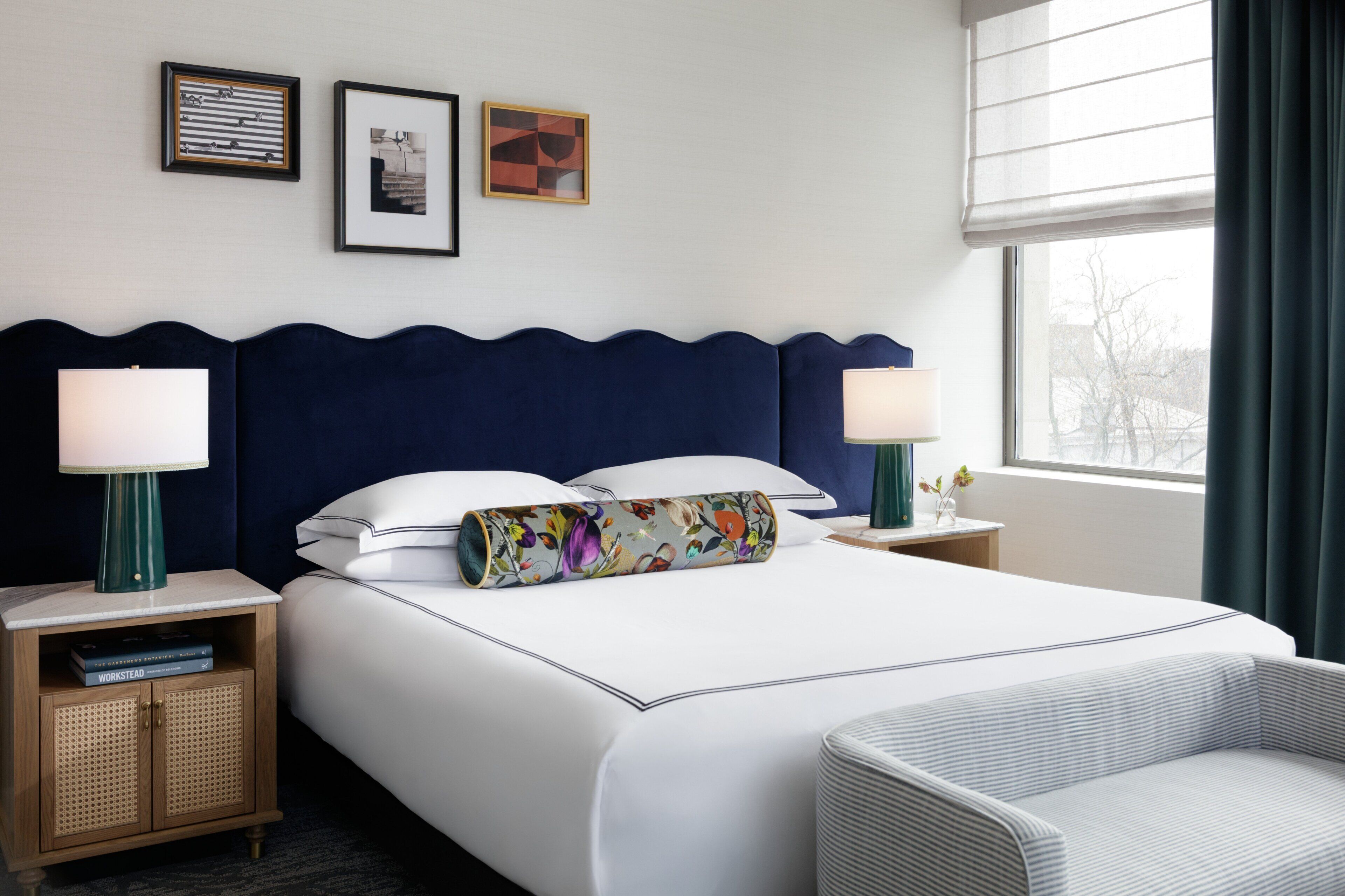 Ein Hotelzimmer mit einem großen Bett, zwei Nachttischen, einem Sessel und einem Fenster mit Vorhängen.