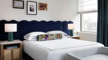 Ein Hotelzimmer mit einem großen Bett, zwei Nachttischen, einem Sessel und einem Fenster mit Vorhängen.