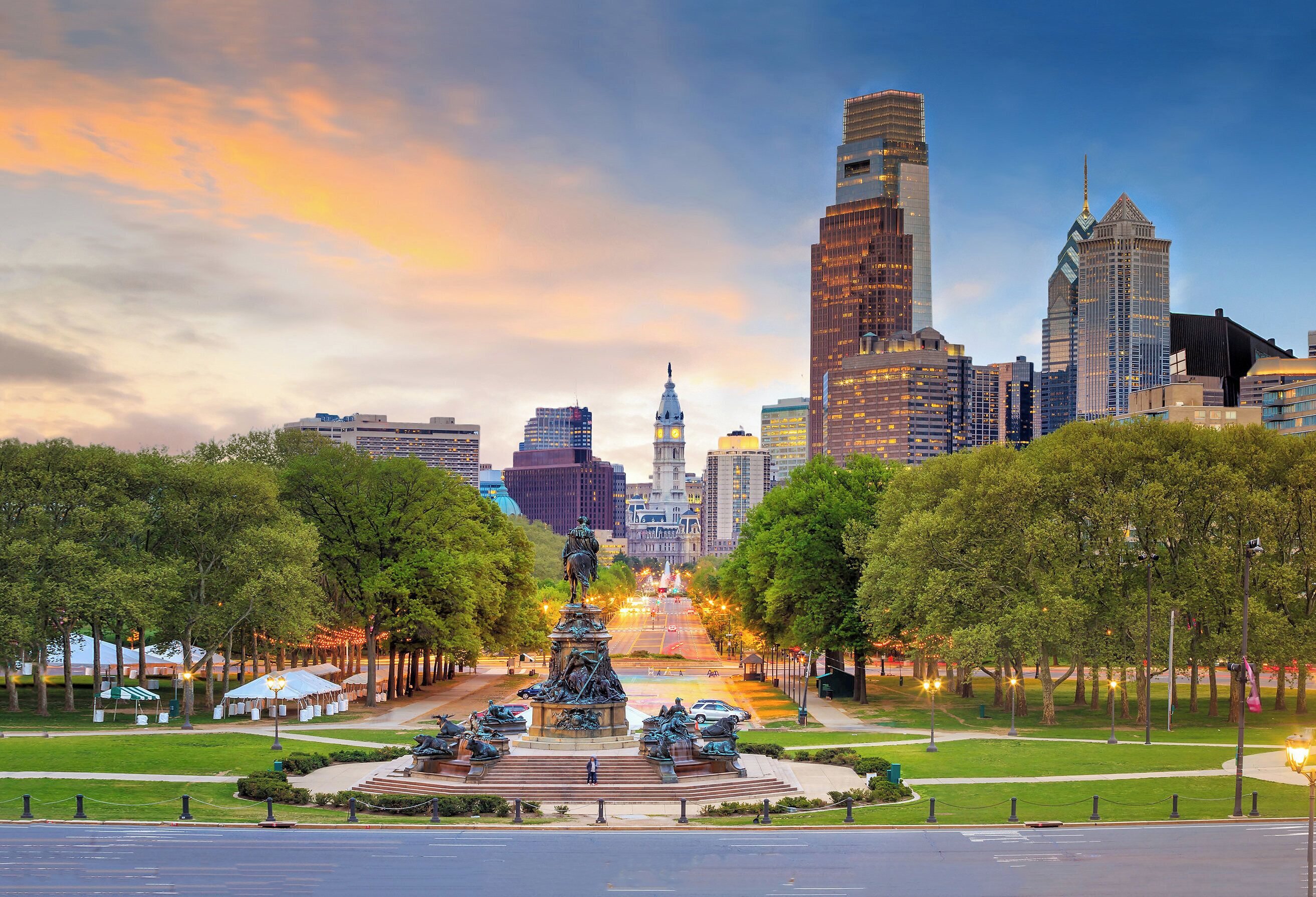 A cityscape with a prominent statue in the foreground, surrounded by trees and a well-maintained park.