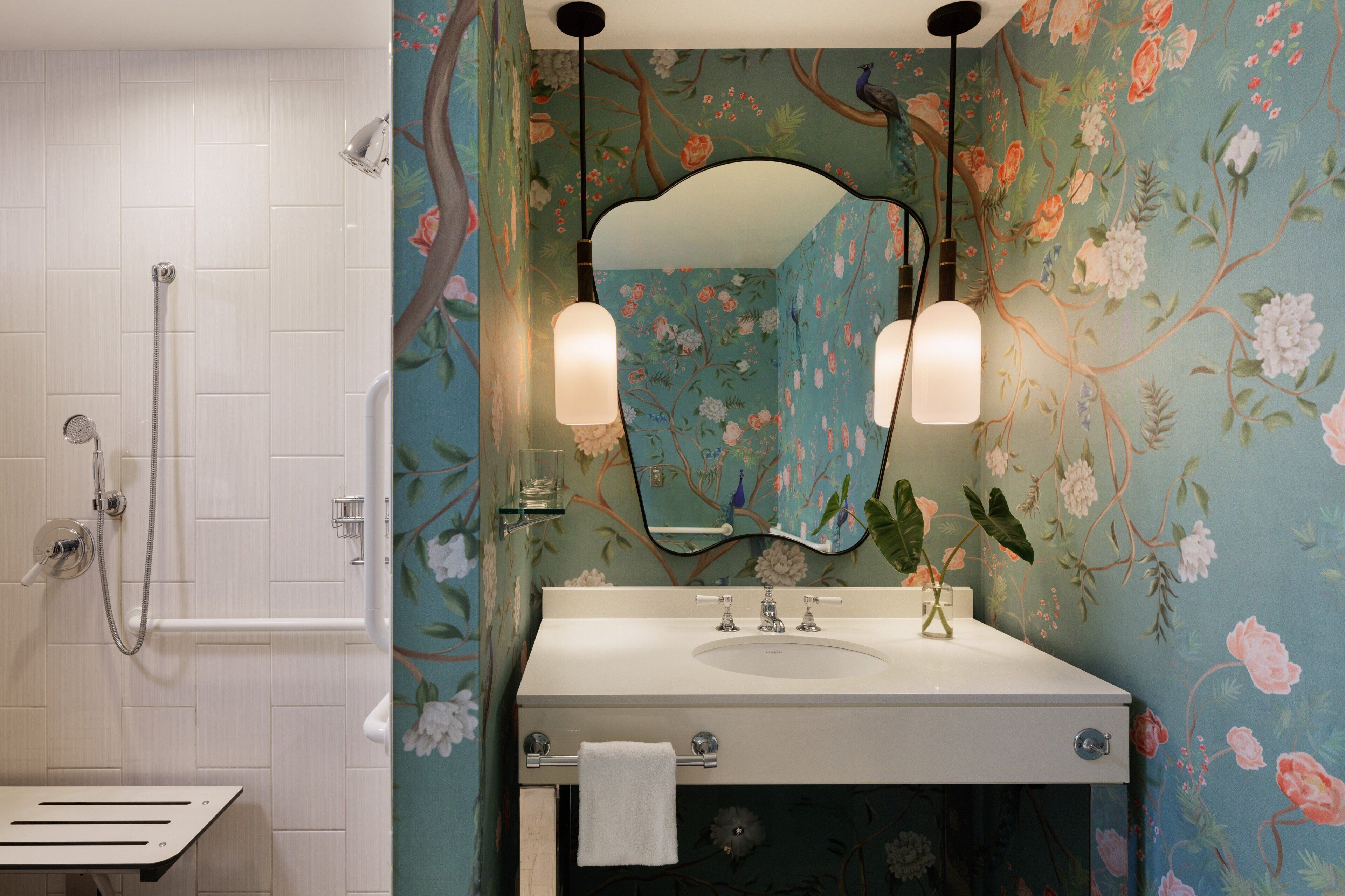 A bathroom with a shower, a sink with a mirror, and floral wallpaper.
