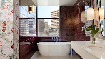A modern bathroom with a freestanding bathtub, a large mirror, and a view of the cityscape through a window.