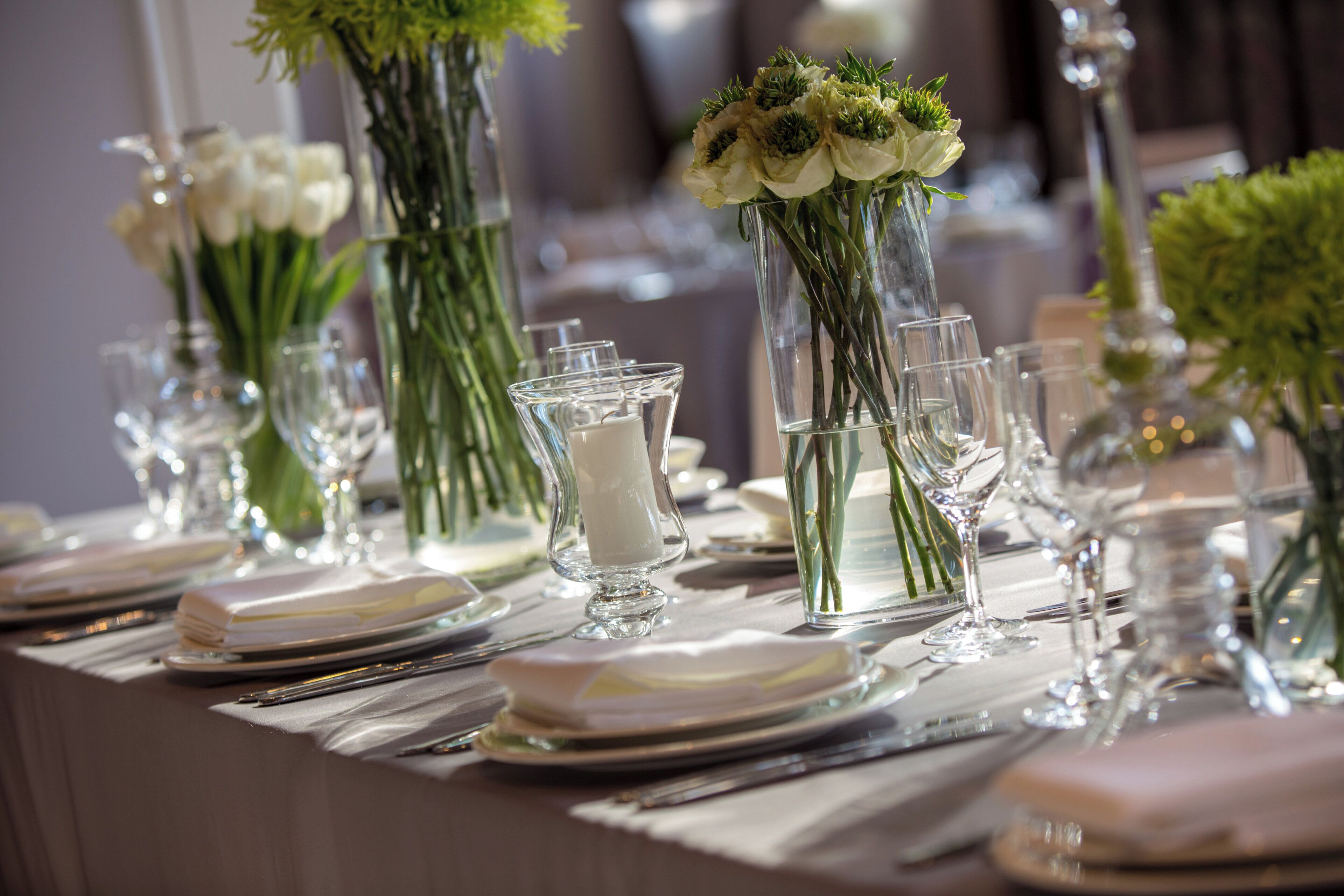 A table set for a formal event with clear glassware, white tablecloths, and floral centerpieces.