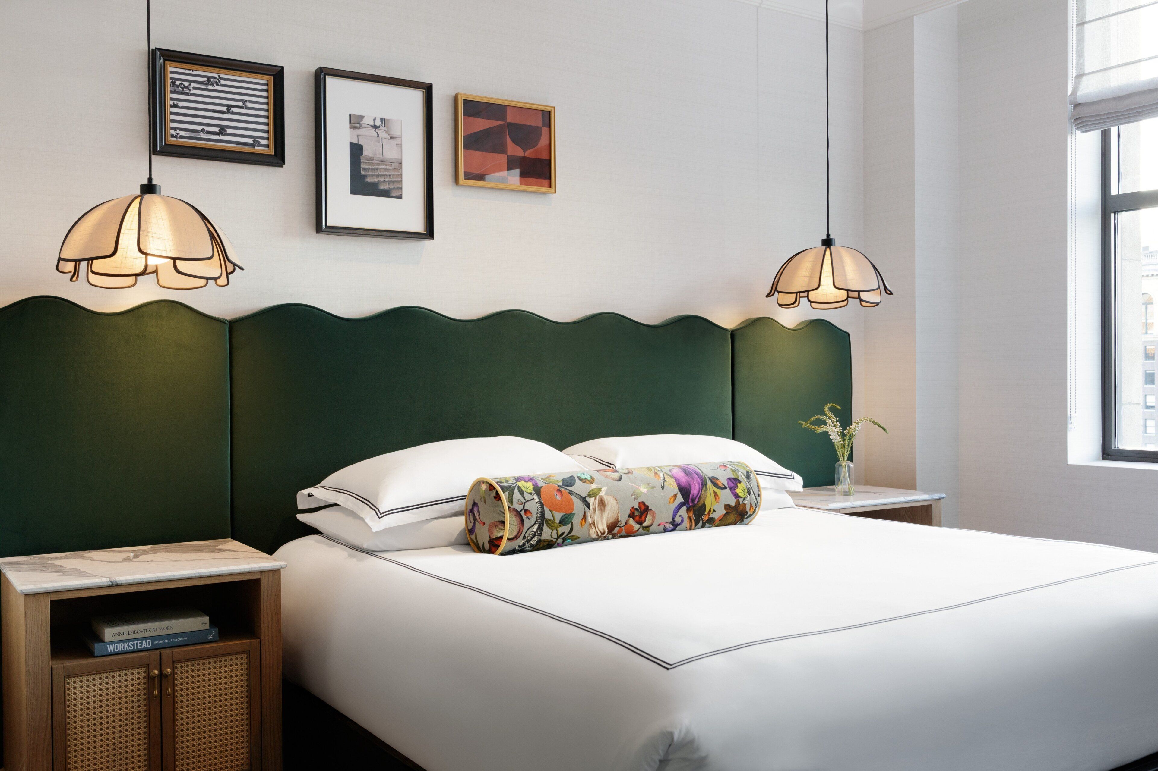 A neatly made bed with a floral pillow, two bedside tables with books, and a vase with flowers on the nightstand.
