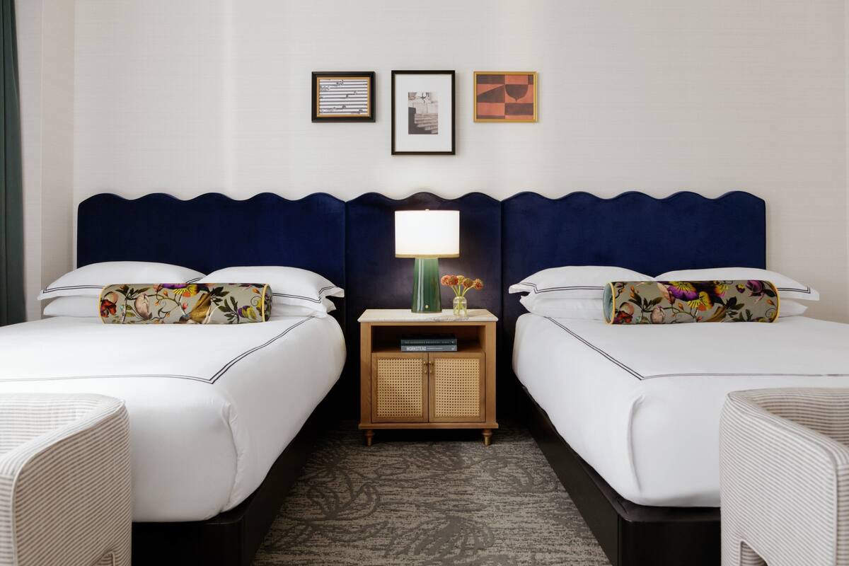 A hotel room with two beds, a nightstand with a lamp, and framed pictures on the wall.