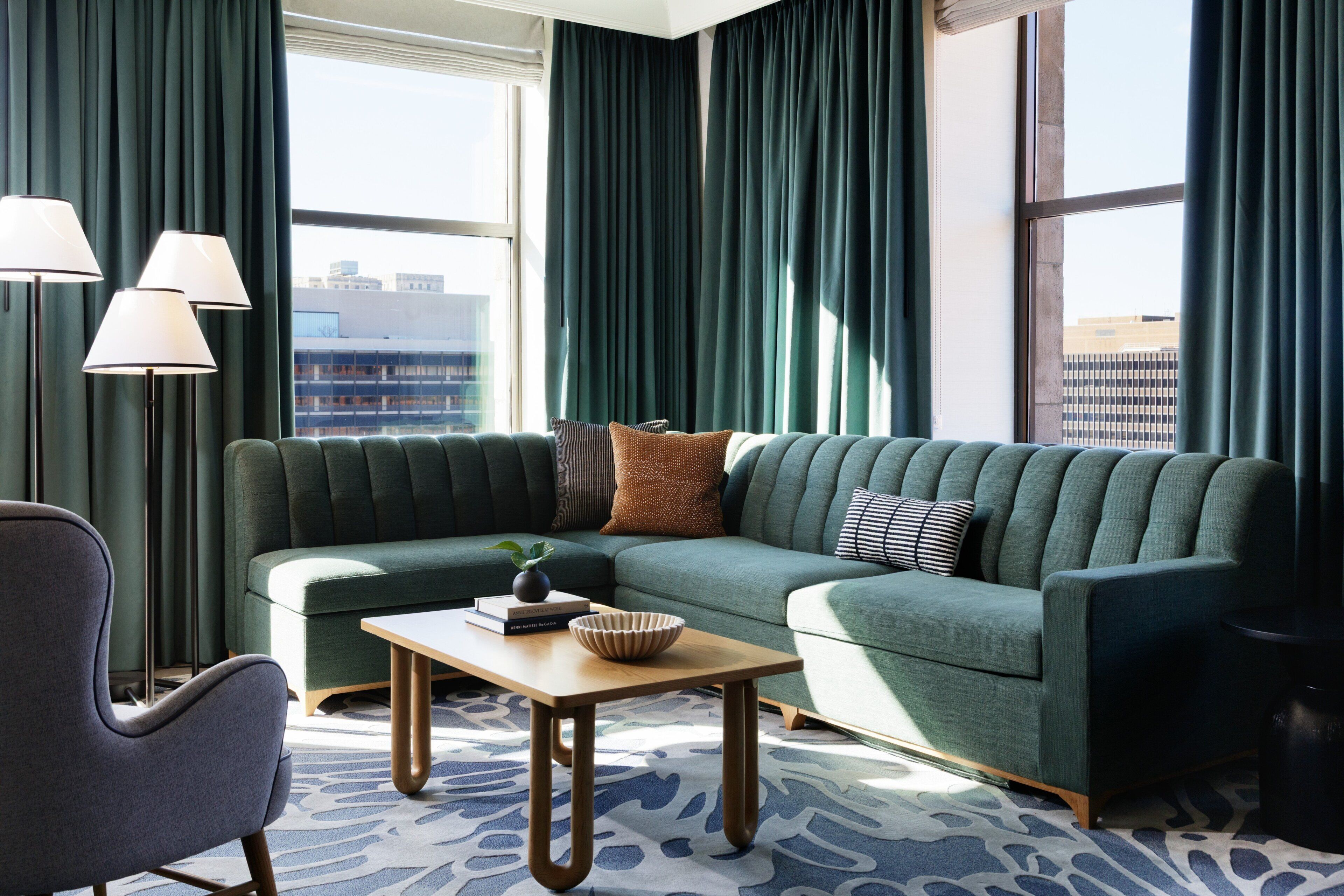 A modern living room with a green sofa, a wooden coffee table, and a view of the cityscape through large windows.
