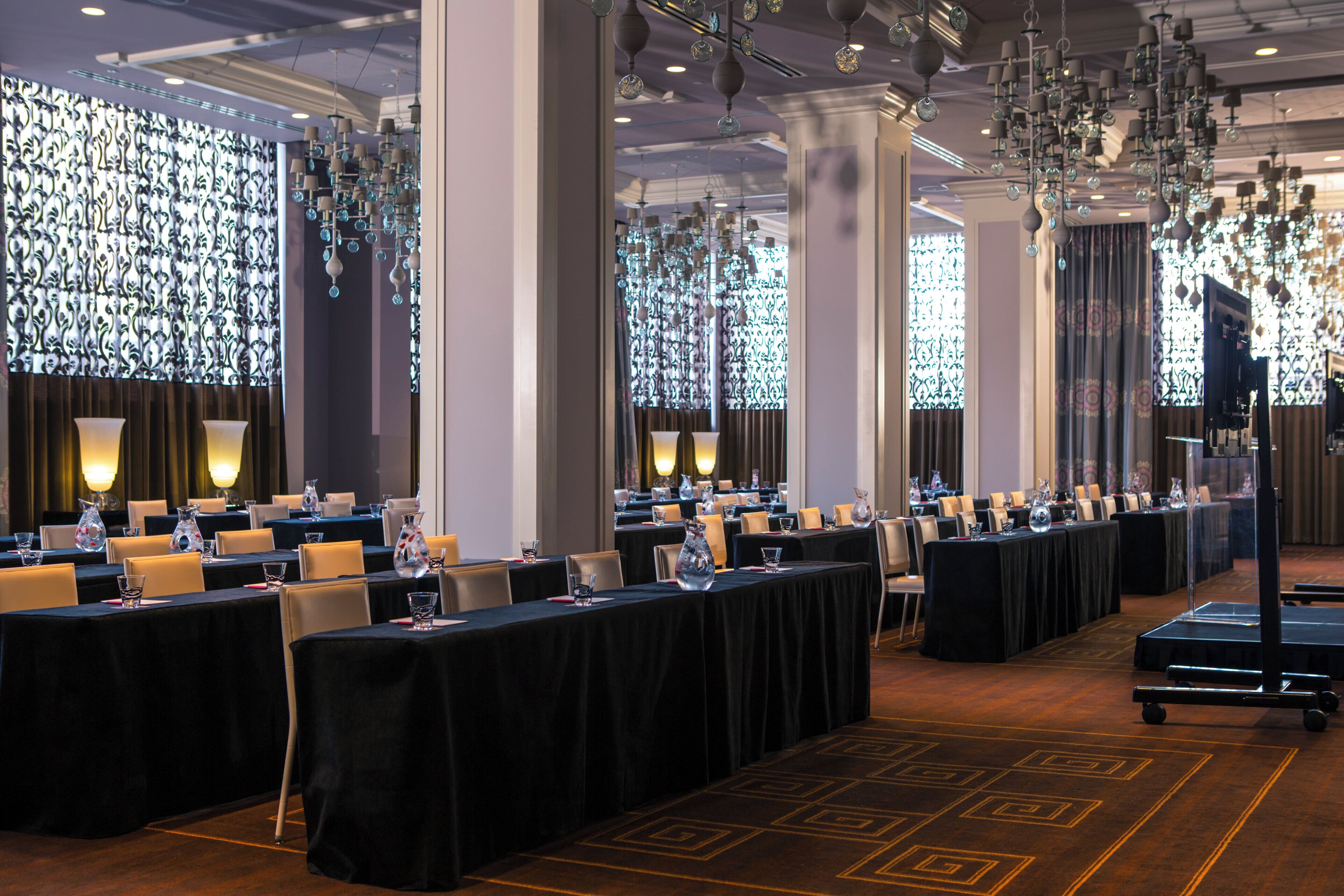 A conference room with tables set for a meeting, large windows with patterned curtains, and hanging decorative lights.