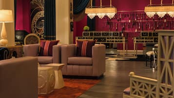 A room with a seating area featuring sofas and a coffee table, a decorative wall with a clock, and a collection of brushes on the wall.