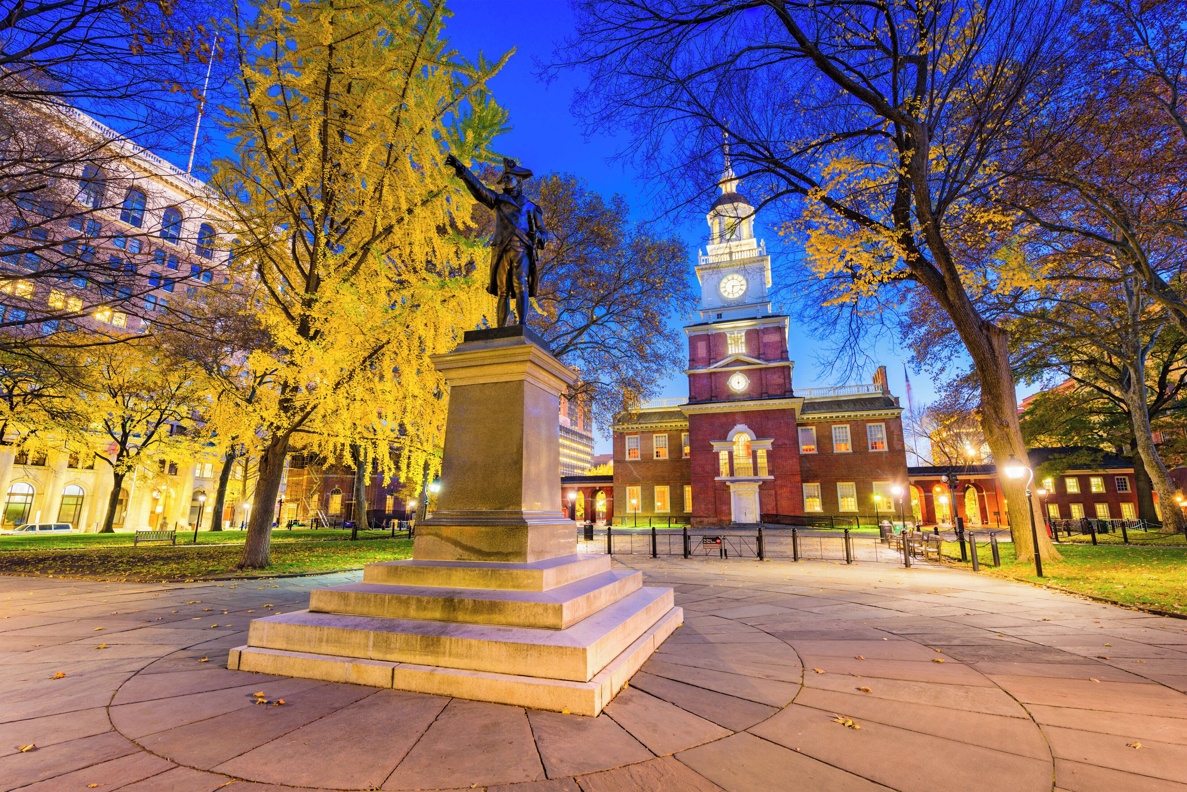 A park with a statue, a clock tower, and a building with a red facade.