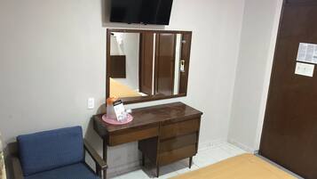 A hotel room with a wooden desk, a chair, a bed, a television, and a wardrobe.