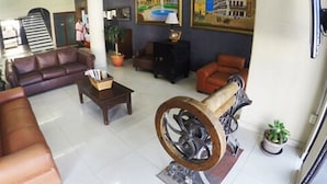 A spacious lobby with a leather sofa, a coffee table, and a large decorative wheel. There are two framed paintings on the wall and a potted plant near the entrance. - Hotel Oriente (Veracruz)