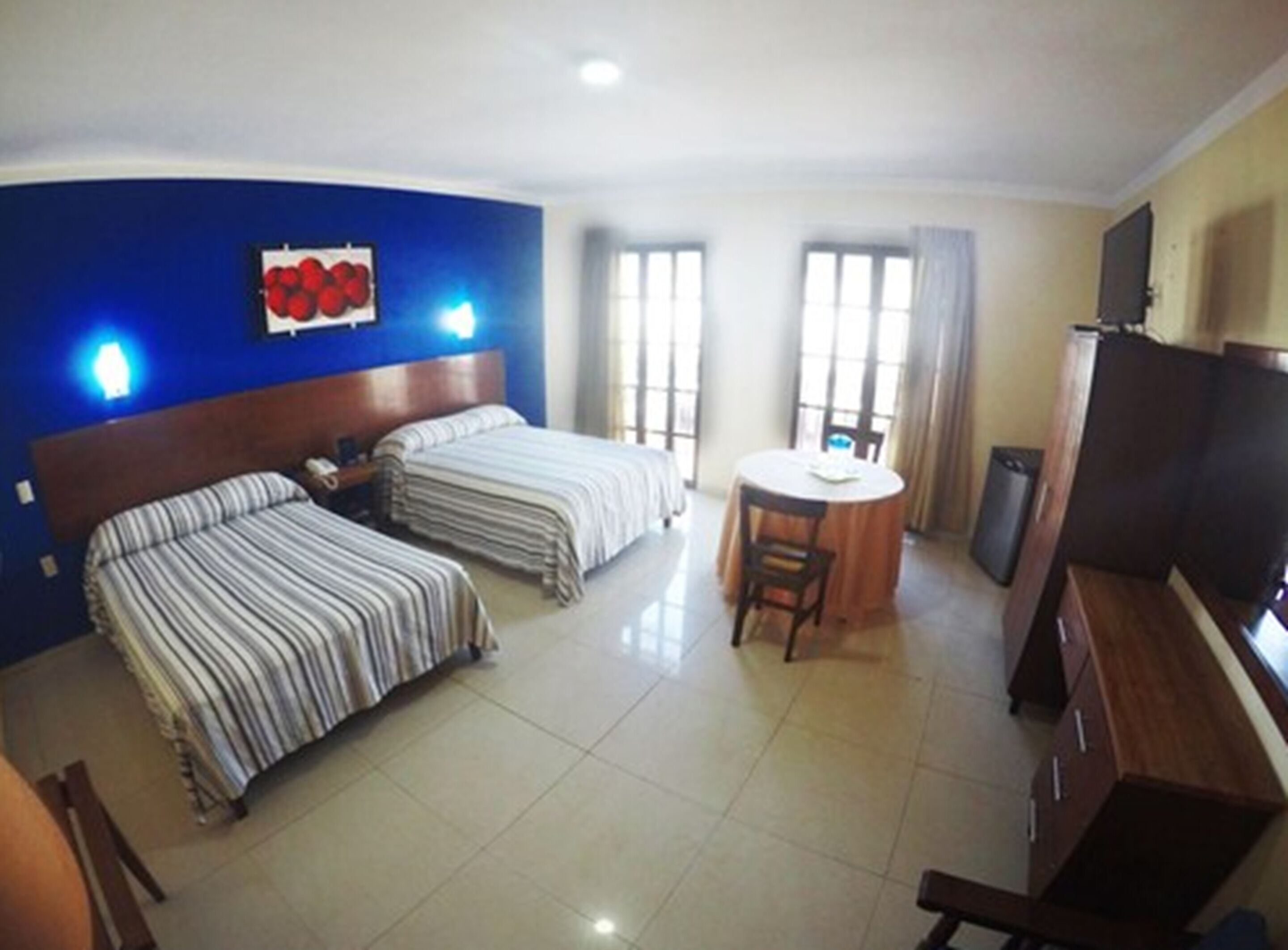 Quarto de hotel com duas camas, uma mesa de jantar e uma televisão.