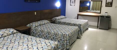 A hotel room with three beds, a desk, a refrigerator, and a wall with framed pictures.