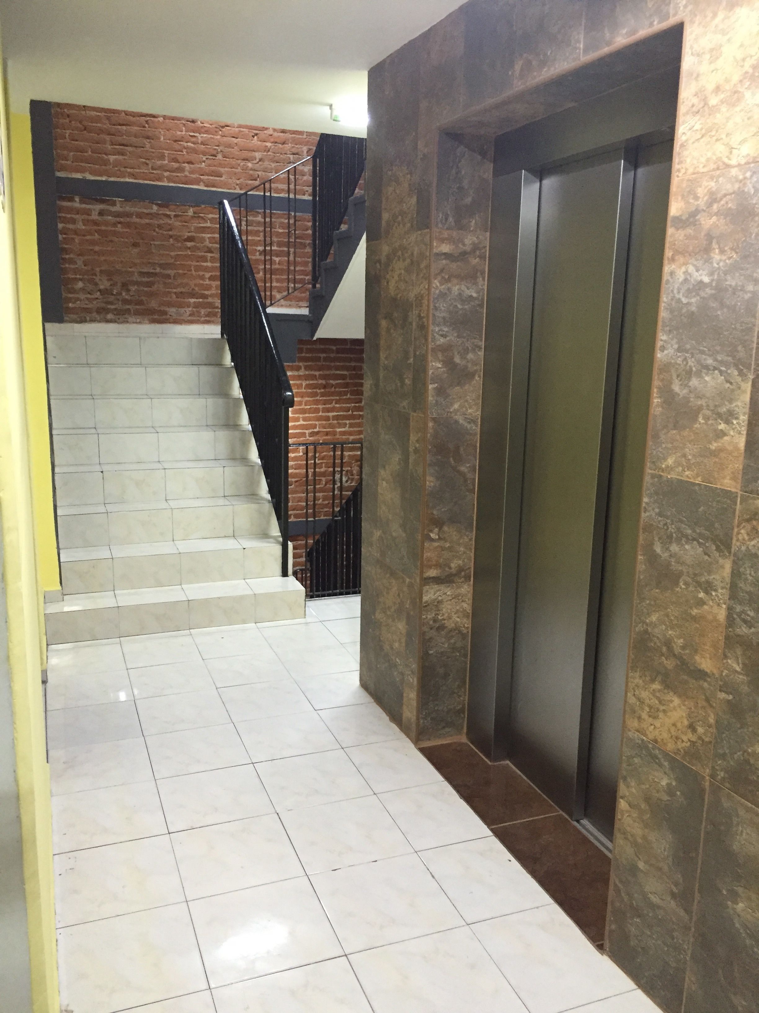 A staircase with a brick wall and a modern elevator.