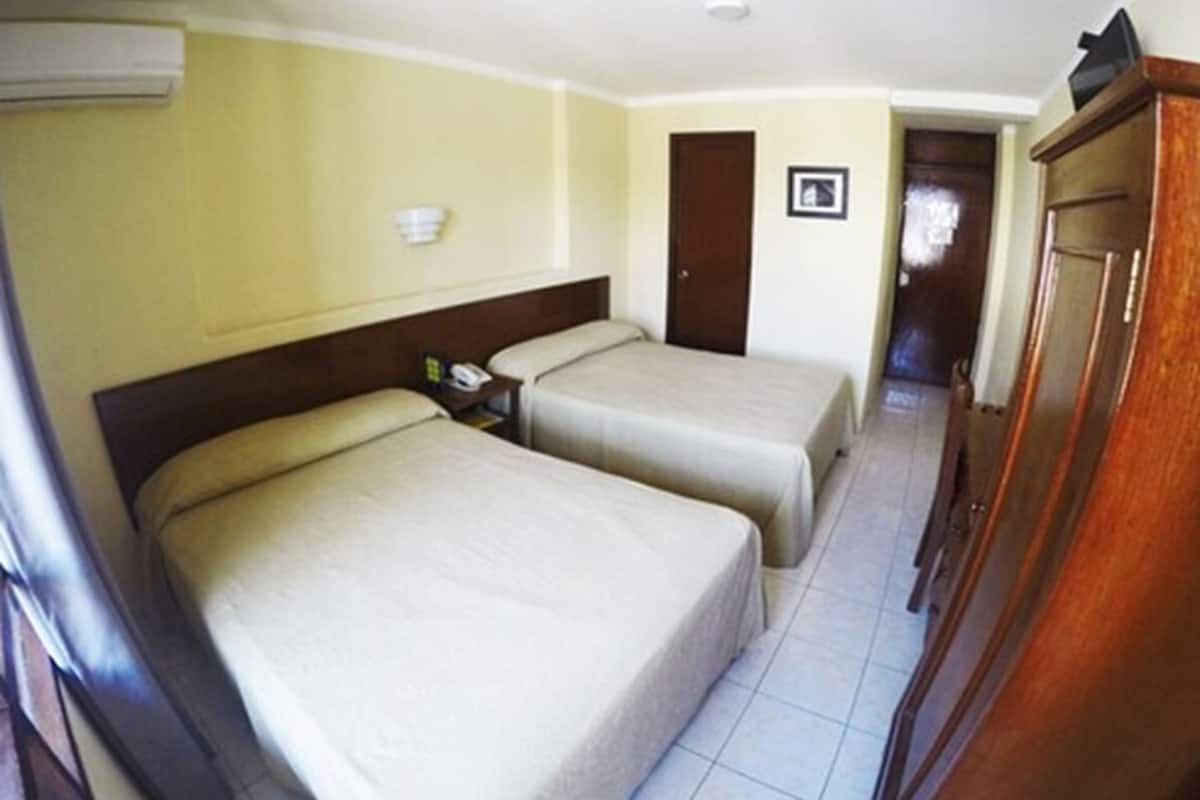 Une chambre d’hôtel avec deux lits, une armoire en bois, une porte et un luminaire fixé au mur.