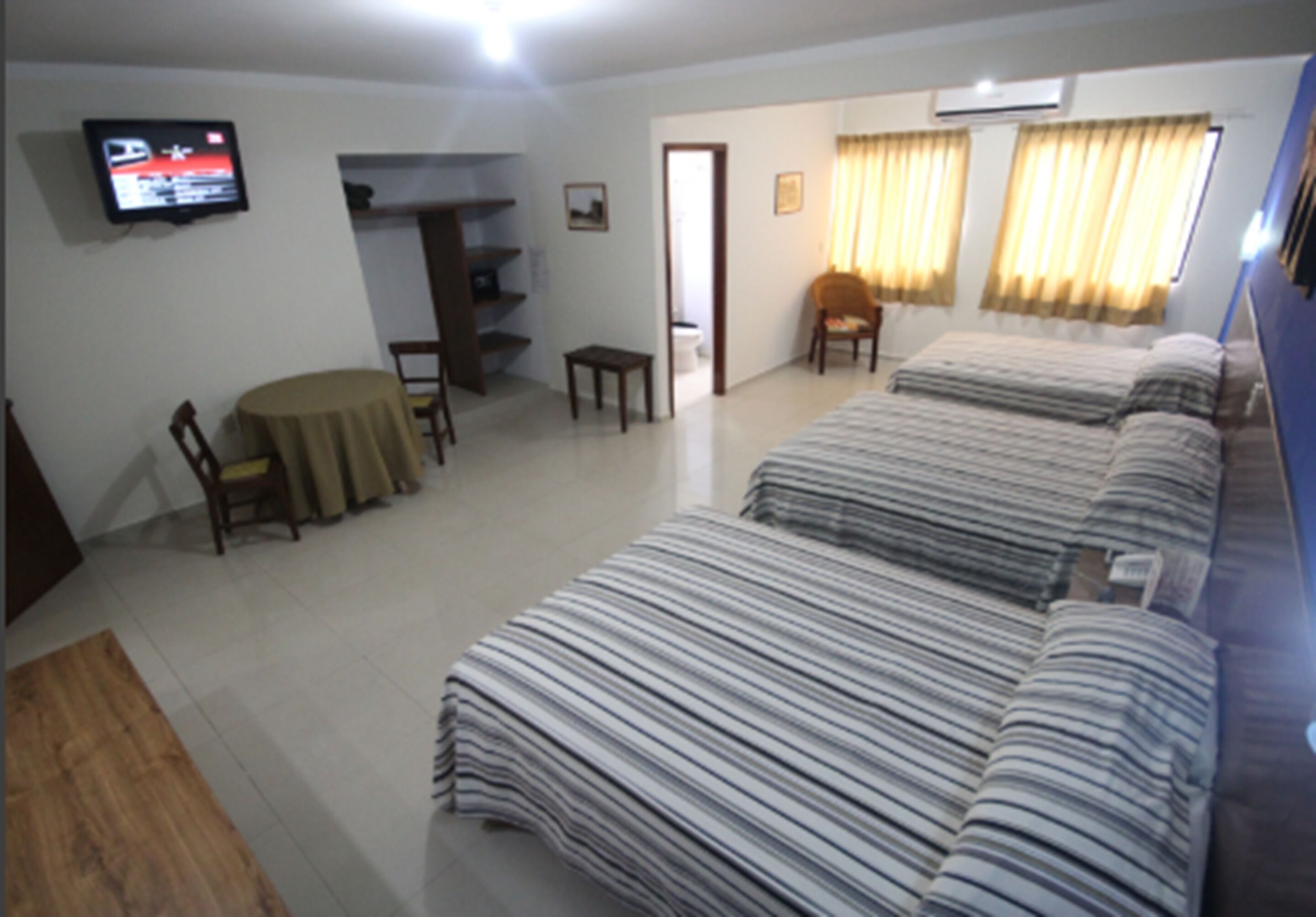 A hotel room with a large bed, a TV mounted on the wall, a small table, and a chair.