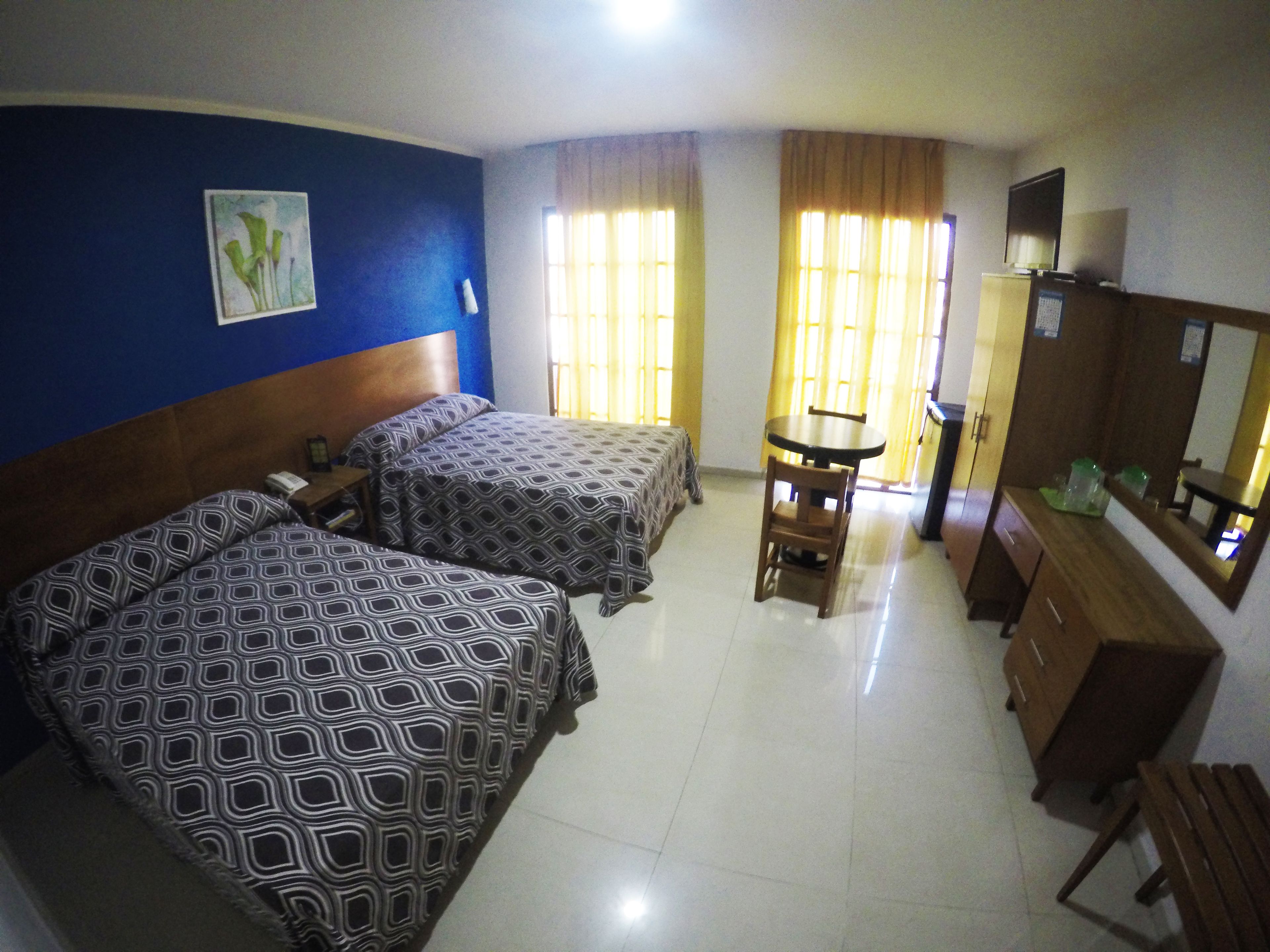 A hotel room with two beds, a desk, a chair, a dresser, and a mirror.