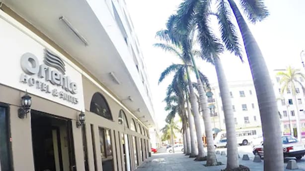 A hotel with a modern facade, palm trees lining the sidewalk, and a clear sky. - Hotel Oriente (Veracruz)