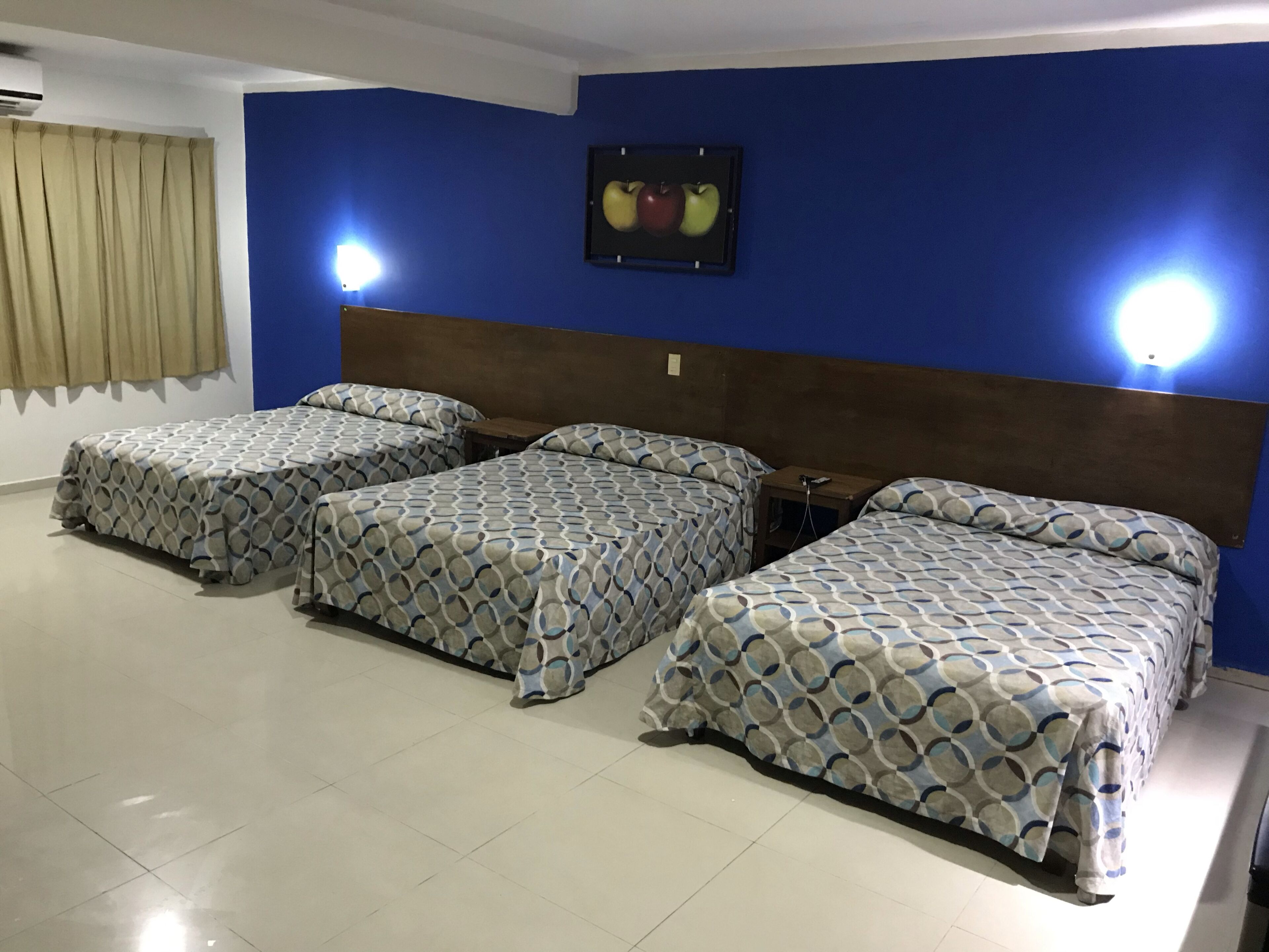 A hotel room with three beds, a blue wall, and a framed picture of apples.
