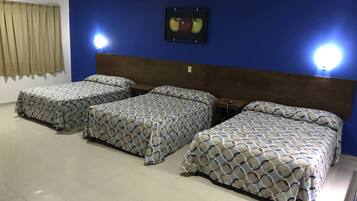 A hotel room with three beds, a blue wall, and a framed picture of apples.